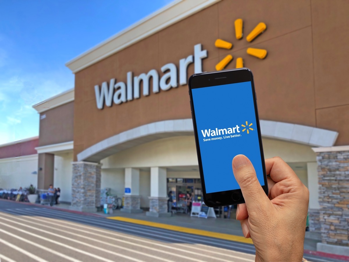 person holding smart phone with walmart app on screen up in front of walmart store