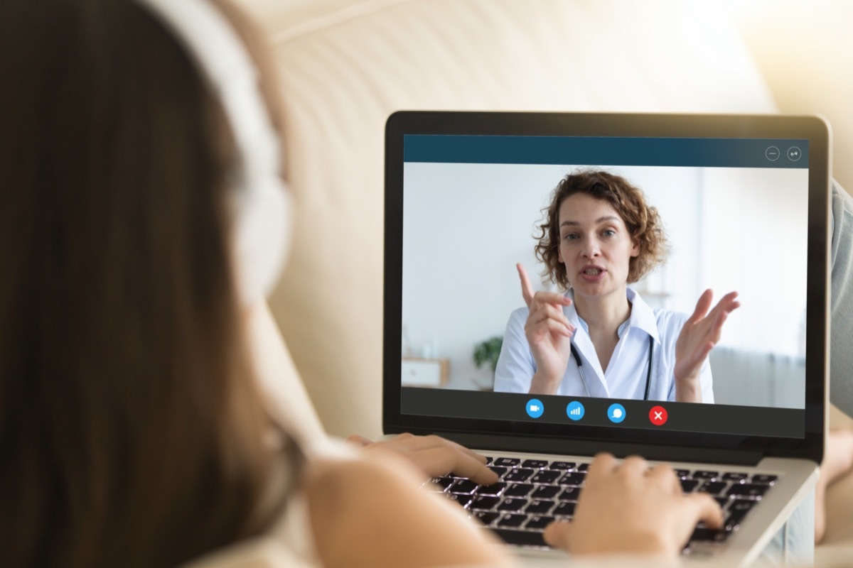 Laptop monitor view over woman shoulder, girl in headphones listens female therapist, medic gives recommendation