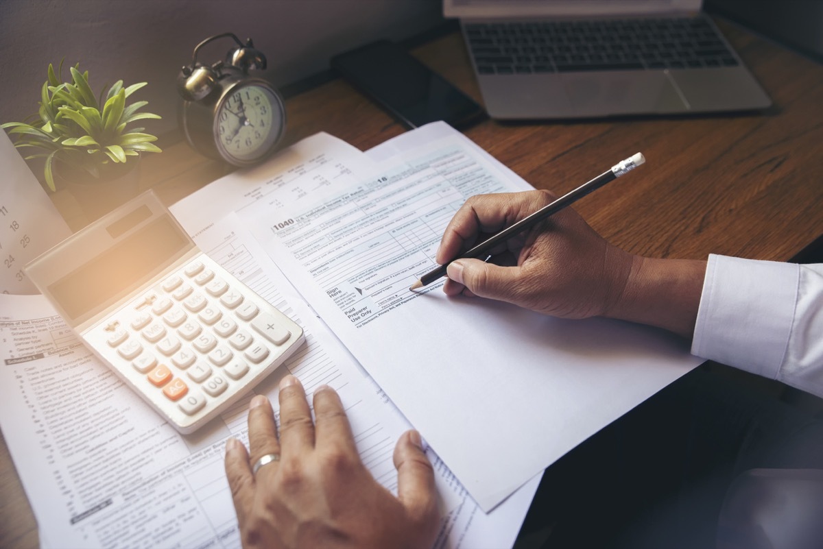 close up of man filling out tax forms with calculator