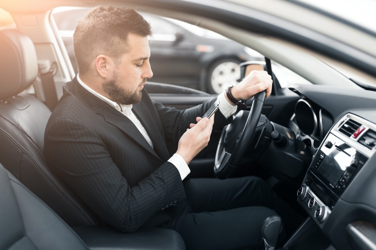 white man in suit looking at phone in car