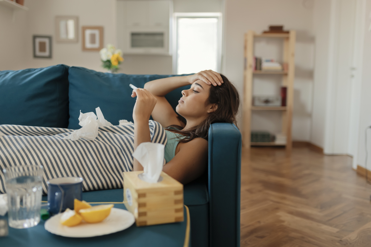 A young woman lying sick on the couch and checking her temperature