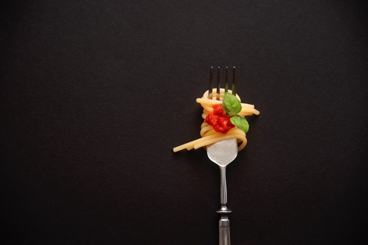 Top view of fork with spaghetti, tomato, and basil on black. Close up. Copy space