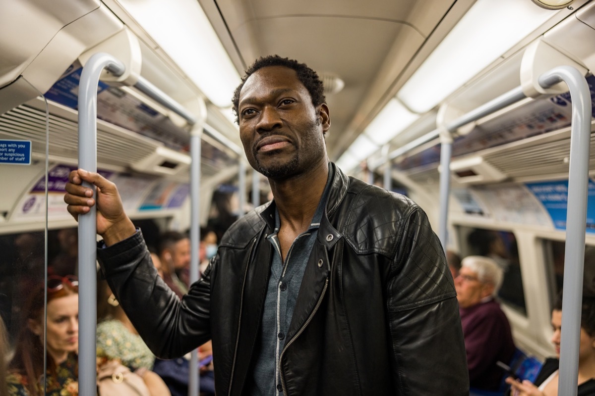 man using public transportation in the city. He is inside a subway metro, standing and holding a pole.