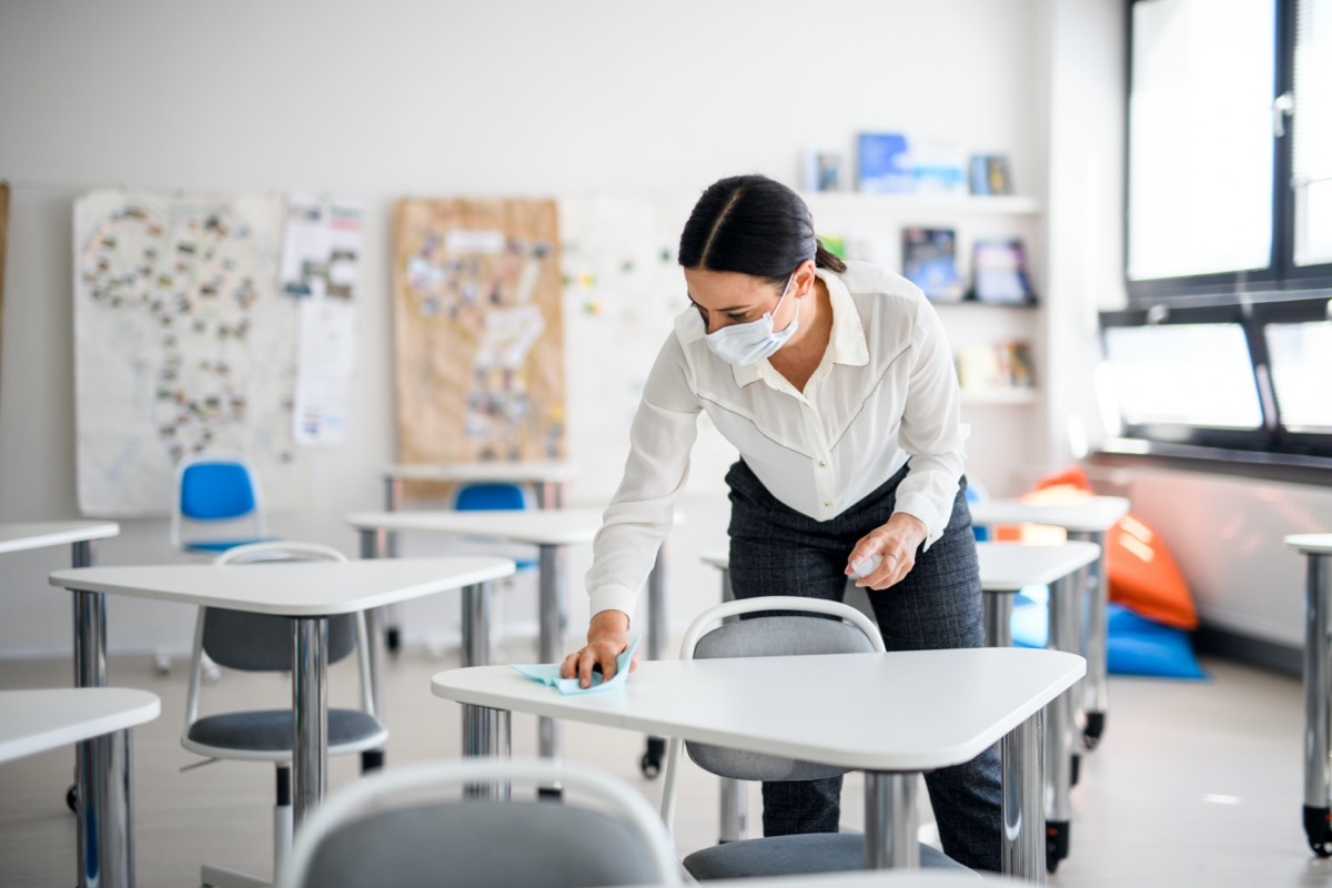 Teacher back at school after covid-19 quarantine and lockdown, disinfecting desks.