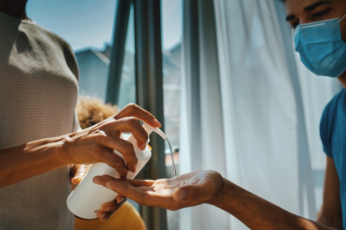 Closeup side view of a woman poring hand sanitizer into her husband's hands. They are next to window,backlit by the sunlight.